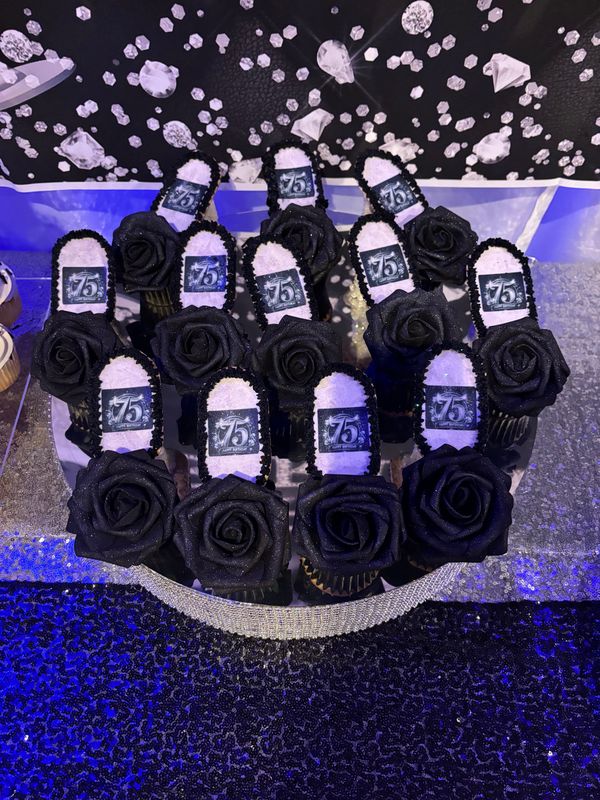 Black rose cupcakes with printed 75th birthday toppers on a dessert table